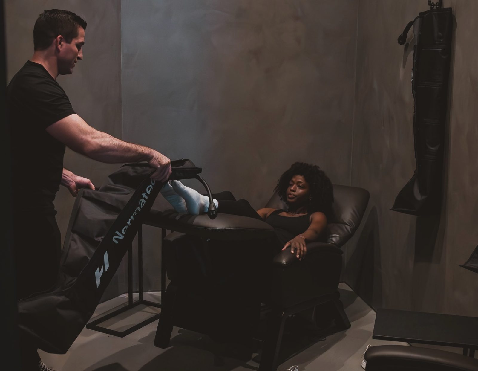 Staff member fitting Normatec compression boots on a guest in a Zero Gravity recliner