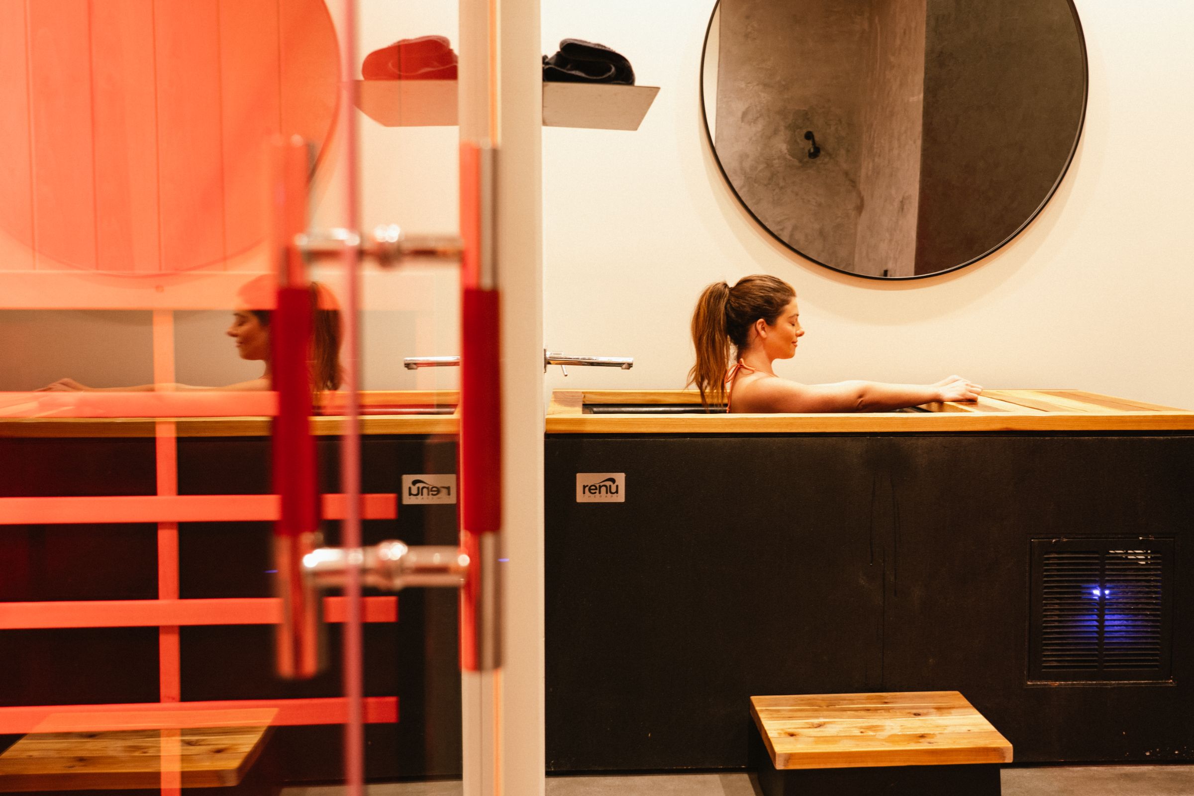 Guest in the cold plunge, seen through the glass door of the infrared sauna