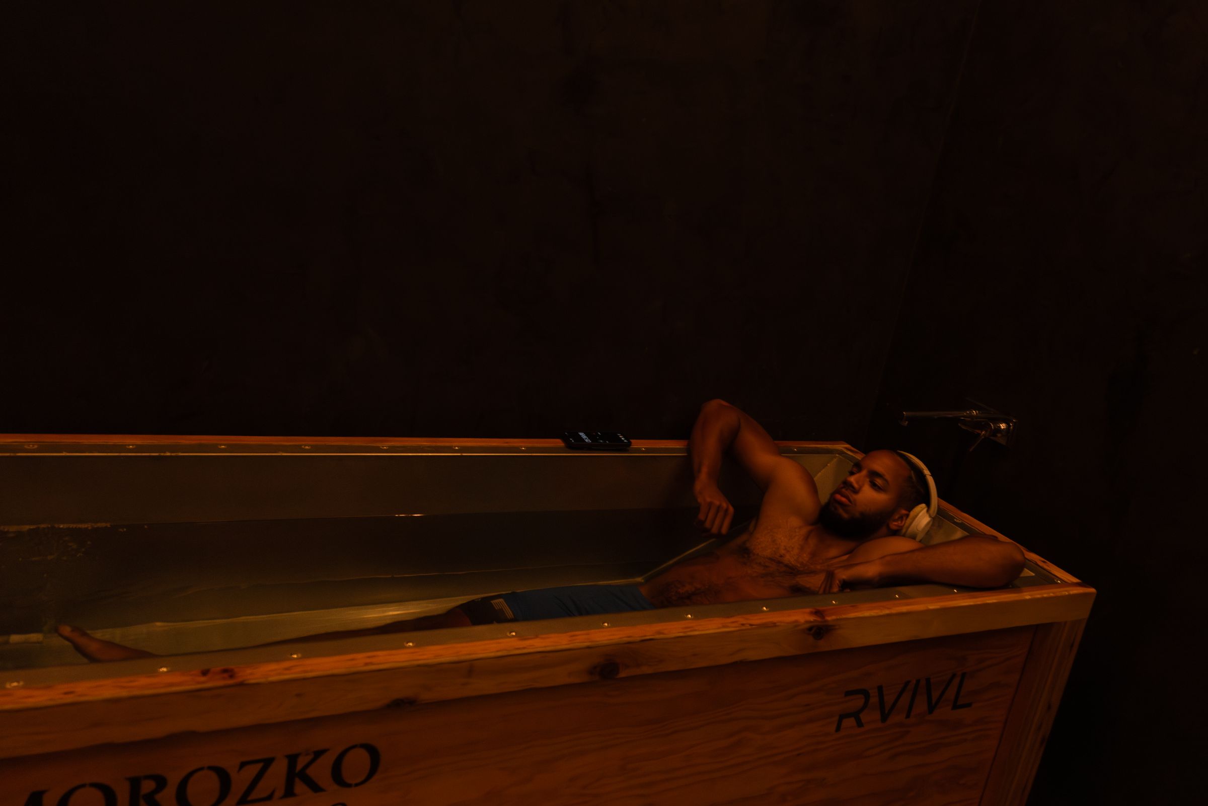 Guest in headphones reclining in the Morozko Forge ice bath